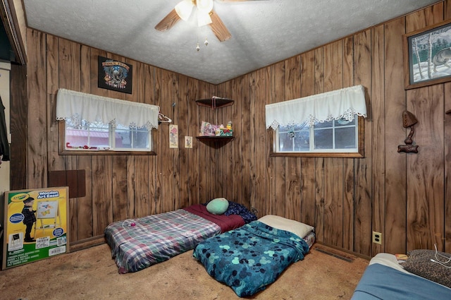 carpeted bedroom featuring ceiling fan, wooden walls, and a textured ceiling