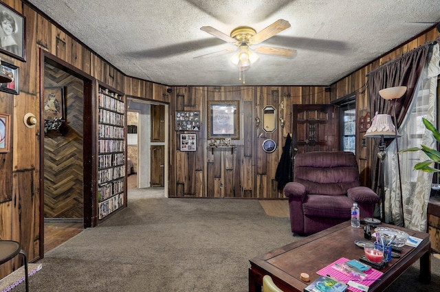 living room featuring ceiling fan, carpet flooring, a textured ceiling, and wood walls