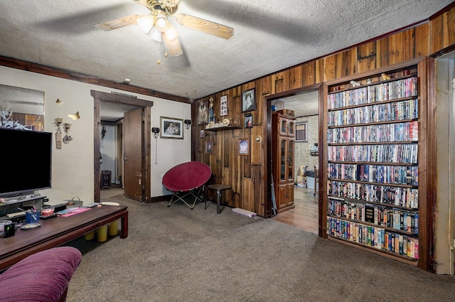 carpeted office featuring ceiling fan, a textured ceiling, and wood walls