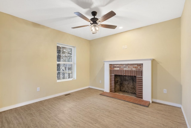 unfurnished living room with ceiling fan, a brick fireplace, and light wood-type flooring