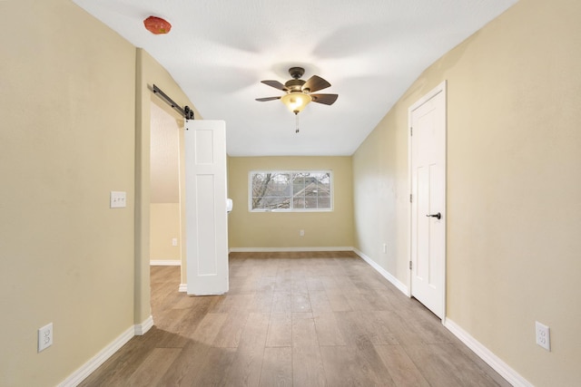 empty room with ceiling fan, a barn door, and light wood-type flooring