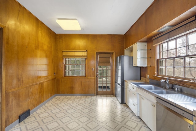 kitchen with appliances with stainless steel finishes, sink, white cabinets, and wood walls