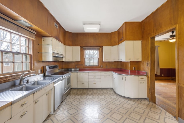 kitchen featuring appliances with stainless steel finishes, wooden walls, sink, white cabinets, and ceiling fan