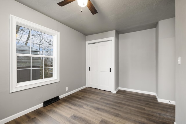 unfurnished bedroom with ceiling fan, dark hardwood / wood-style flooring, a closet, and a textured ceiling