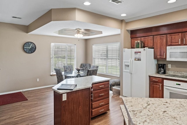 kitchen with hardwood / wood-style floors, a center island, ceiling fan, light stone counters, and white appliances