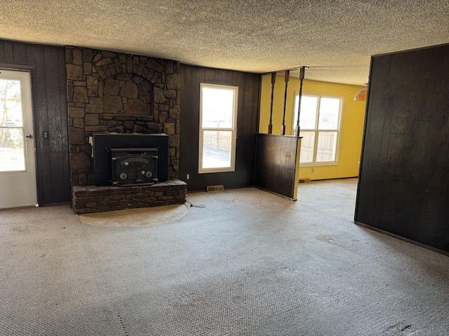 unfurnished living room with wooden walls, light colored carpet, and a textured ceiling