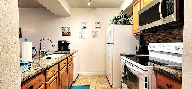 kitchen with sink, white appliances, stone counters, decorative backsplash, and light wood-type flooring