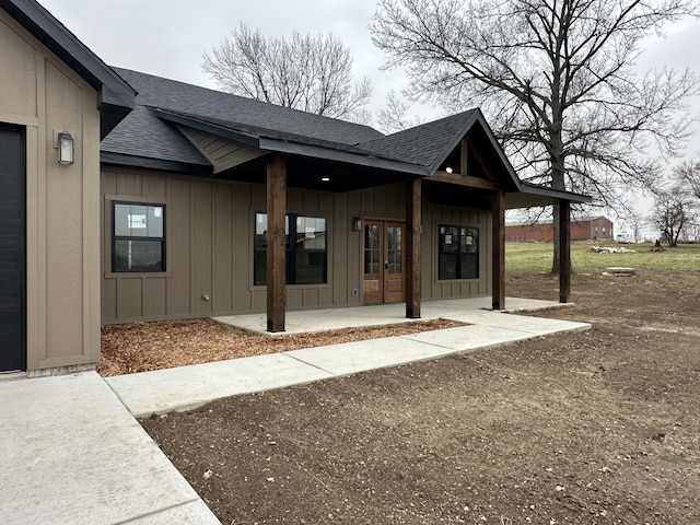 entrance to property with board and batten siding, a shingled roof, french doors, and a patio