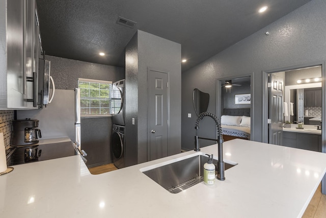 kitchen with lofted ceiling, sink, stacked washer and dryer, backsplash, and kitchen peninsula