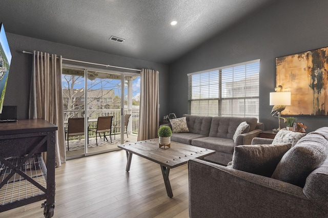 living room with lofted ceiling, light hardwood / wood-style flooring, and a textured ceiling