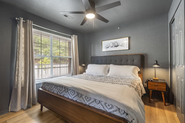 bedroom featuring ceiling fan, light hardwood / wood-style floors, and a textured ceiling