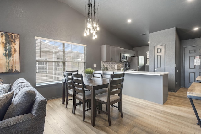 dining room with high vaulted ceiling, a healthy amount of sunlight, an inviting chandelier, and light hardwood / wood-style flooring