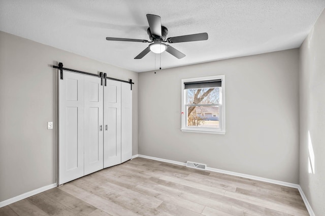 unfurnished bedroom with a barn door, baseboards, light wood-type flooring, and a closet