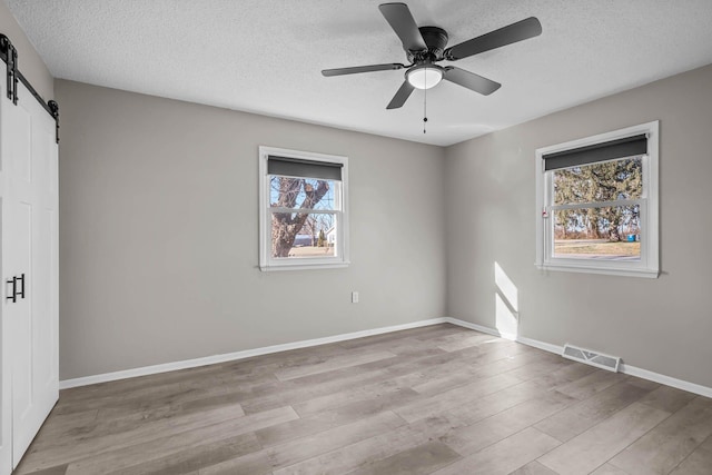 unfurnished bedroom featuring visible vents, a barn door, baseboards, and wood finished floors