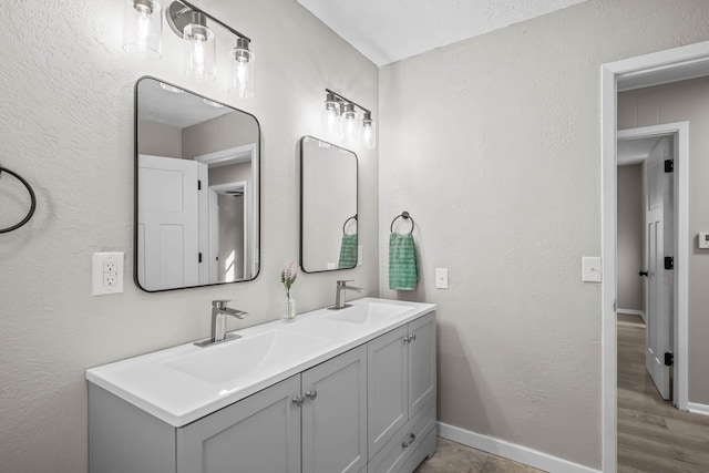 bathroom featuring a sink, baseboards, double vanity, and a textured wall