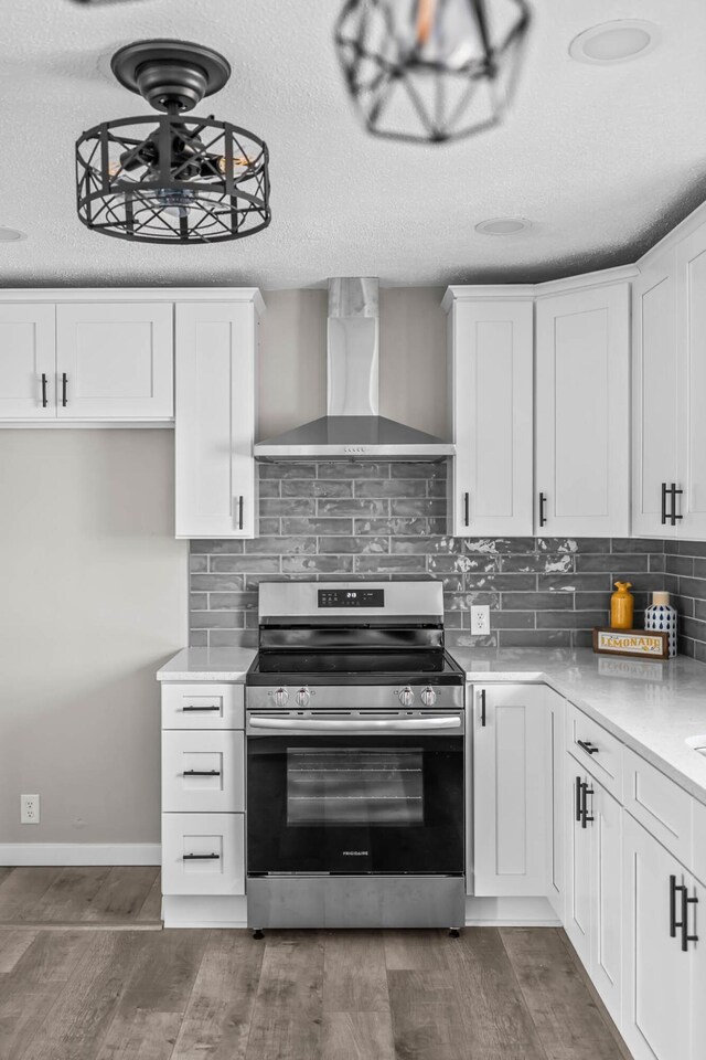 kitchen featuring tasteful backsplash, wall chimney range hood, wood finished floors, electric range, and white cabinetry