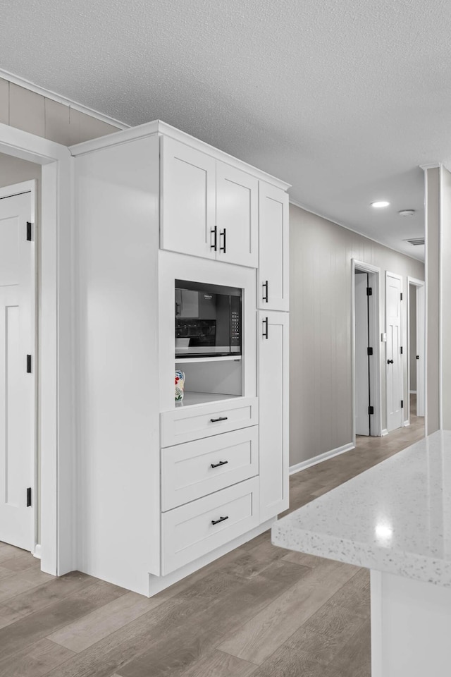 kitchen with built in microwave, a textured ceiling, white cabinets, and light wood finished floors