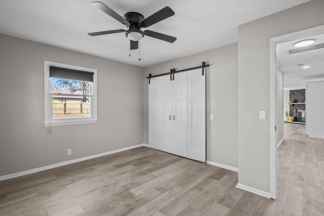 unfurnished bedroom with visible vents, baseboards, light wood-type flooring, a barn door, and a fireplace