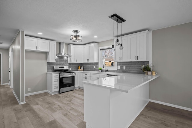 kitchen featuring a peninsula, light wood-style flooring, stainless steel electric stove, a sink, and wall chimney exhaust hood