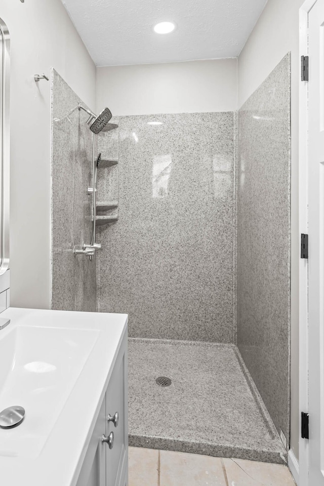 full bath featuring a tile shower, tile patterned flooring, a textured ceiling, and vanity