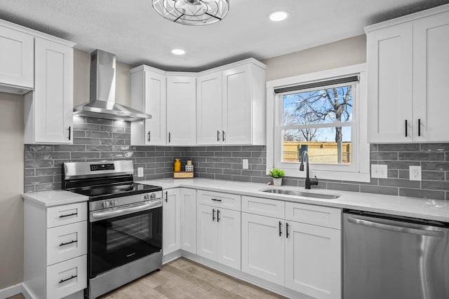 kitchen featuring stainless steel appliances, wall chimney exhaust hood, light countertops, and a sink