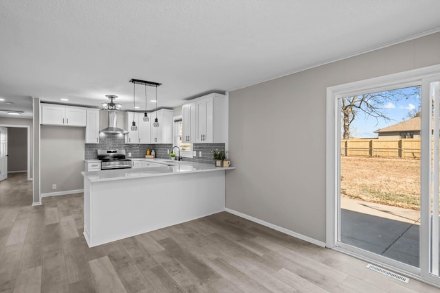 kitchen featuring visible vents, stainless steel electric range, a peninsula, wall chimney range hood, and decorative backsplash