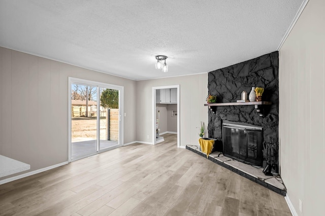 living room with a stone fireplace, a textured ceiling, baseboards, and wood finished floors