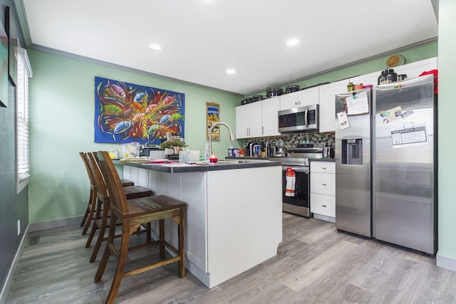 kitchen with sink, a breakfast bar, stainless steel appliances, light hardwood / wood-style floors, and white cabinets