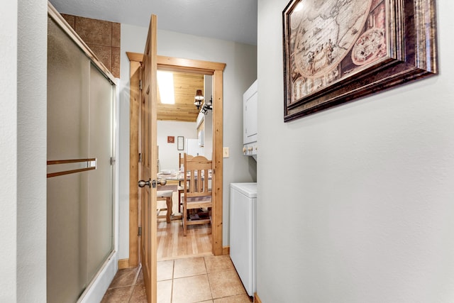 corridor featuring stacked washing maching and dryer and light tile patterned floors