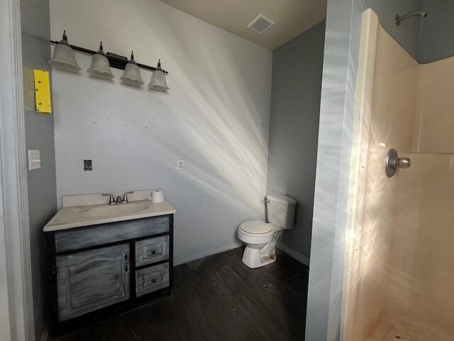 bathroom with hardwood / wood-style flooring, vanity, toilet, and a shower