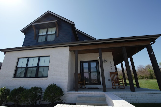 view of front of home featuring brick siding, french doors, and covered porch