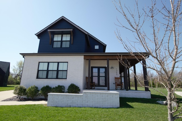 view of front of house featuring covered porch, a front yard, and brick siding