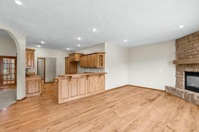 kitchen featuring a breakfast bar area, light hardwood / wood-style floors, a textured ceiling, a stone fireplace, and kitchen peninsula