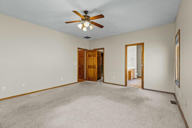 unfurnished bedroom featuring light carpet, a walk in closet, ceiling fan, and ensuite bathroom