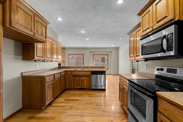 kitchen with appliances with stainless steel finishes, a textured ceiling, light wood-type flooring, and kitchen peninsula