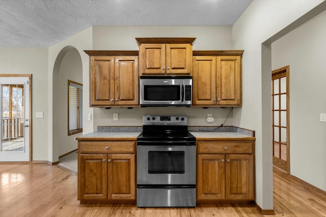 kitchen featuring light wood-type flooring, a textured ceiling, and appliances with stainless steel finishes