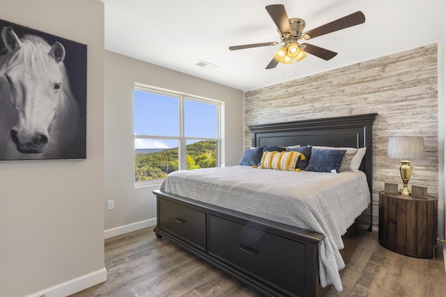 bedroom with an accent wall, wood finished floors, visible vents, and baseboards
