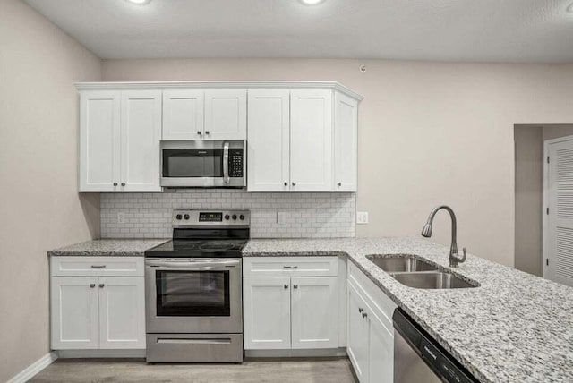 kitchen featuring light stone counters, a sink, white cabinets, appliances with stainless steel finishes, and decorative backsplash