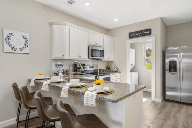 kitchen with light stone counters, stacked washer and clothes dryer, stainless steel appliances, white cabinetry, and a kitchen breakfast bar