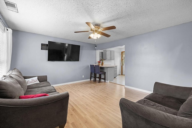 living room with ceiling fan, light hardwood / wood-style floors, and a textured ceiling