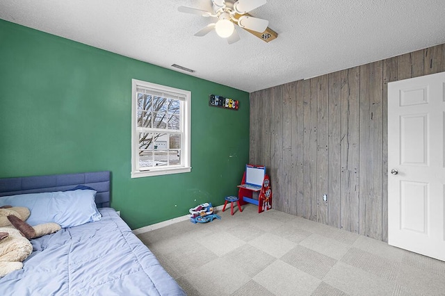 bedroom featuring ceiling fan, wooden walls, carpet, and a textured ceiling