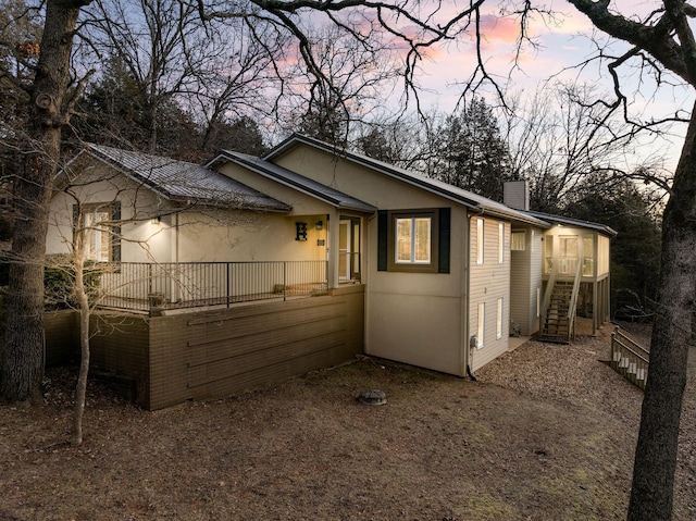 property exterior at dusk featuring stairs, a chimney, and stucco siding