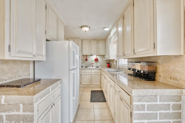 kitchen with light tile patterned flooring, sink, white fridge, decorative backsplash, and cream cabinetry