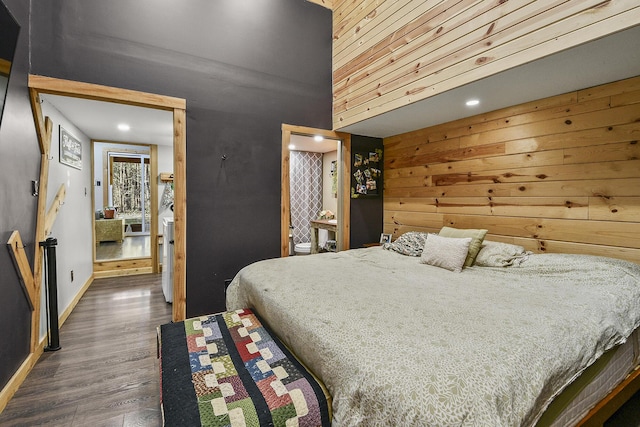 bedroom with a towering ceiling, ensuite bath, dark hardwood / wood-style flooring, and wood walls