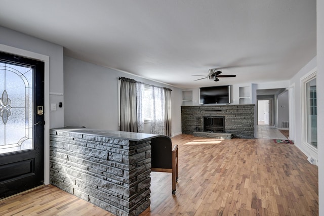 interior space with ceiling fan, a stone fireplace, and light hardwood / wood-style floors