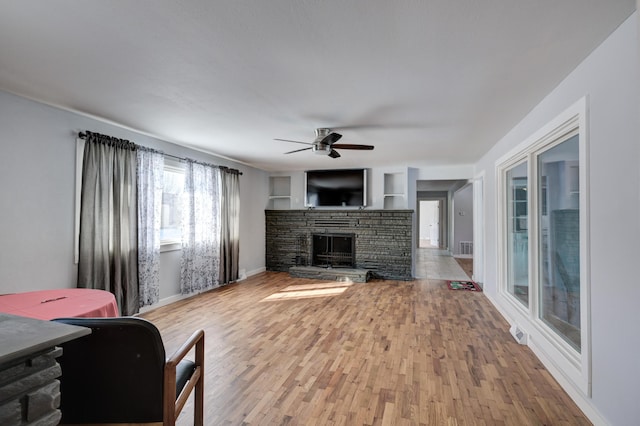 living room featuring hardwood / wood-style flooring, ceiling fan, a fireplace, and built in shelves