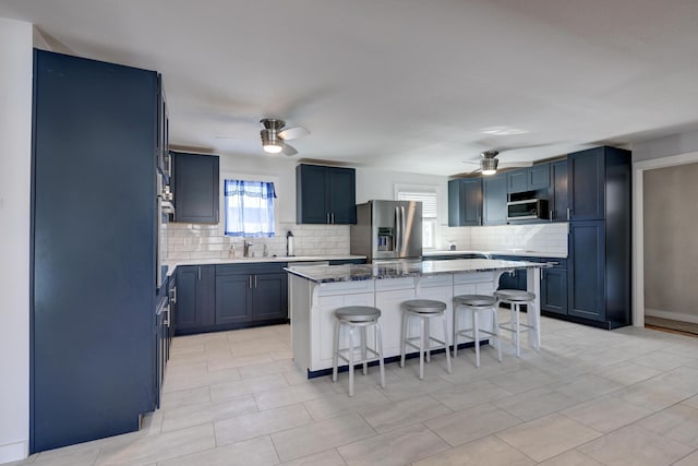 kitchen featuring a breakfast bar area, ceiling fan, appliances with stainless steel finishes, light stone countertops, and a kitchen island