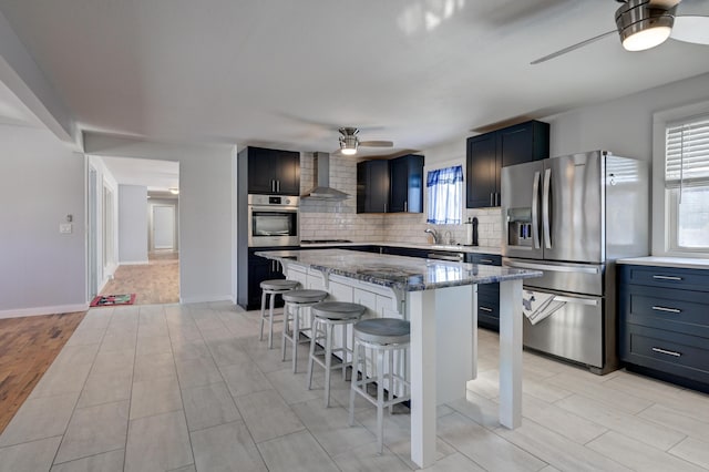 kitchen featuring wall chimney range hood, a breakfast bar area, stainless steel appliances, a center island, and dark stone counters