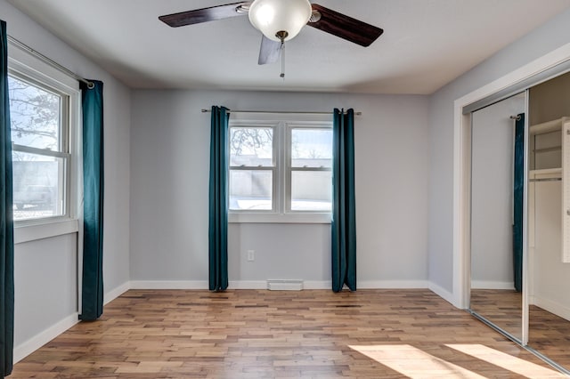 unfurnished bedroom featuring ceiling fan, a closet, light hardwood / wood-style floors, and multiple windows