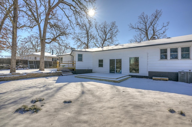 snow covered back of property featuring central AC unit and a patio